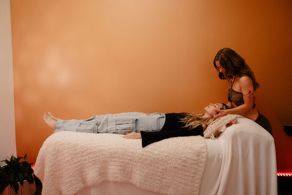 Woman receiving kinesiology and reiki from another woman in a warmly lit room.